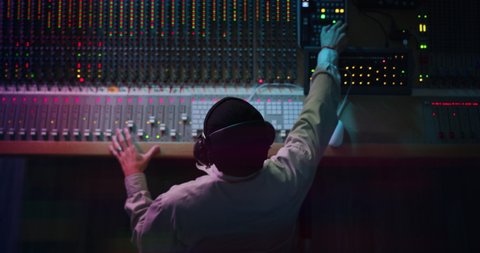Cinematic top view of professional male sound producer with headphones is recording a new song with young singer in a music studio with colorful lights on a background.