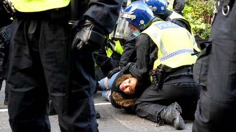 LONDON, ENGLAND, UNITED KINGDOM - 28, NOVEMBER, 2020: Riot policemen wearing helmets and bright vests holding young woman tightly on the ground surrounded by other officers in Regent Street.