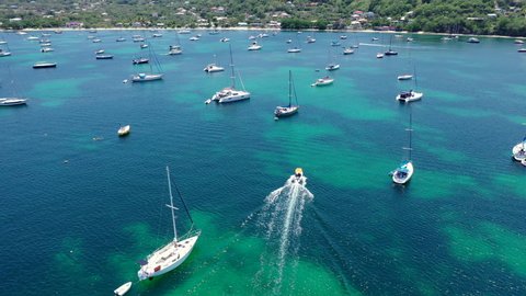 Aerial, pov, a small motor boat among anchored sailboats off the coast of an island, Grenada