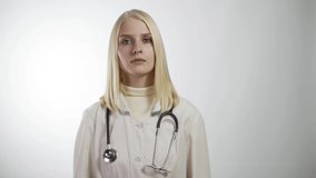 video portrait of happy smiling female doctor in white coat with stethoscope showing thumbs up over grey background