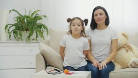 4k slowmotion video of mother and daughter on white sofa posing for a video.
