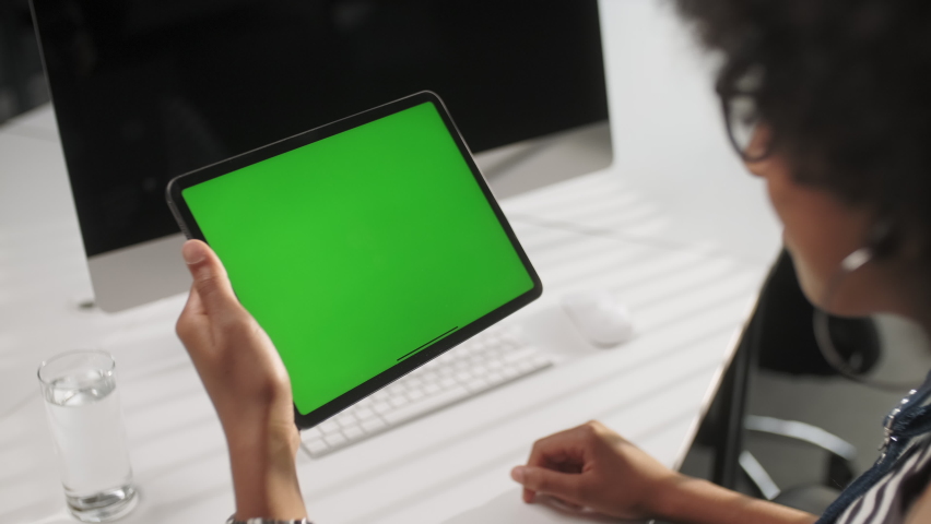 View From the Shoulder of Woman Holding and Using Hand Gestures Swipe Up on Green Mock-up Screen Digital Tablet Computer Sitting at The Desk. Browsing the Internet. Background Office. Royalty-Free Stock Footage #1063703767