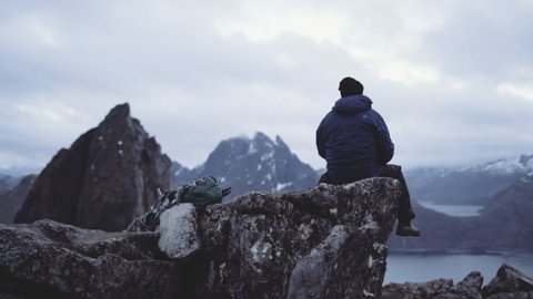 Tracking Wide Shot Of Lone Hiker Resting With Hot Drink On Rocky Outcrop Looking At View Of Segla Mountain And Fjords, Norway