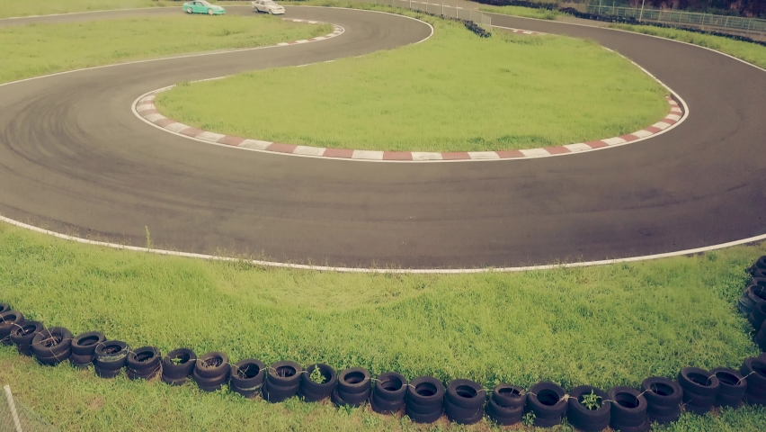 Two high performance cars drifting or sliding around hairpin turn of race track. Tilt up shot.