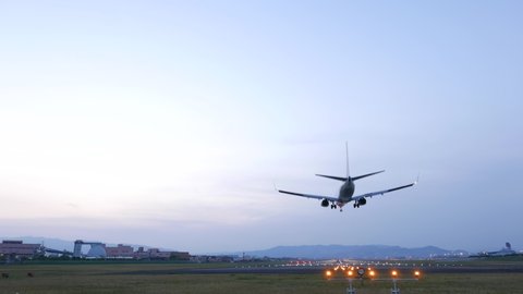 Jet liner landing at Itami airport in evening time, wide angle shot from end of runway. Passenger plane pass by over and move down, touch ground and roll to airport
