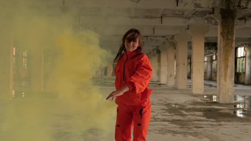 Stylish woman with smoke in hand dancing in abandoned factory. Freestyle dance improvisation. Young carefree woman in orange wear enjoys dancing in 4K, UHD | Shutterstock HD Video #1063717483