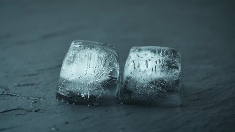 Time lapse of melting two blue ice cubes on dark stone plate. UHD 4k timelapse