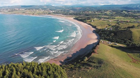 Aerial drone shot of the Cantabrian coast through San Vicente de la Barquera and the Oyambre Natural Park. Mountains and green cliffs by the sea, where you will find famous beaches for surfing. Waves