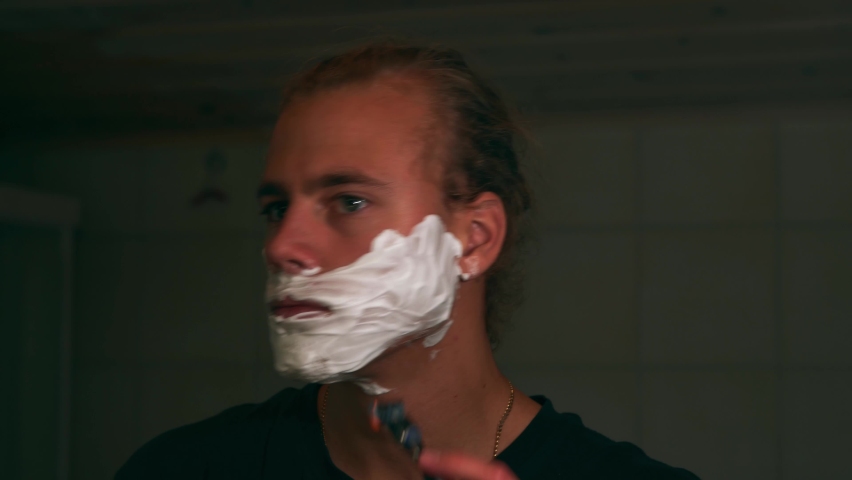 Young man shaving beard with shaving foam and a razor.
