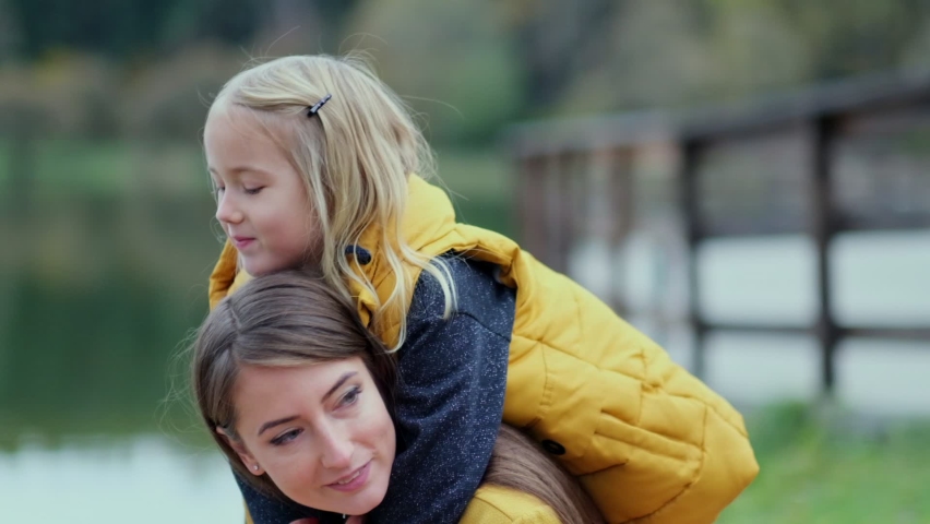 Beautiful and happy young mother giving piggyback ride to her laughing daughter. Slow motion video. stock footage