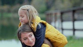 Beautiful and happy young mother giving piggyback ride to her laughing daughter. Slow motion video. stock footage