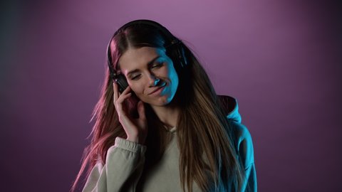 Slow motion of young woman listening music with neon lights background. Filmed on high speed cinema camera.
