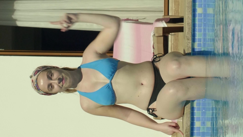 Woman by the pool gesturing to scroll the phone screen.Video for the vertical story.