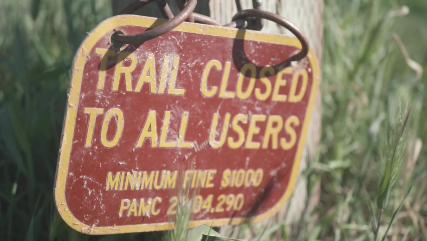 Trail Closed sign on a chain, hanging on a fence post in the grass at Arastradero Preserve in Palo Alto, California. It