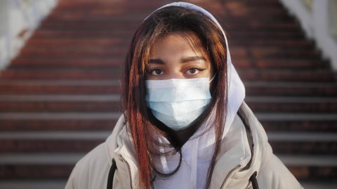 Portrait of beautiful black young woman wearing protective medical face mask and Standing on the street. Teenager practicing social distancing, quarantine, air pollution.