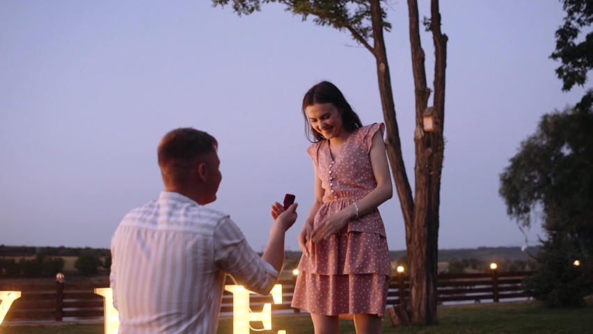 An emotional moment in which a young man asks his girlfriend for marriage. Romantic couple. Concept of marriage applications in nature. Merry me out of the lights. He said yes. Royalty-Free Stock Footage #1063731529