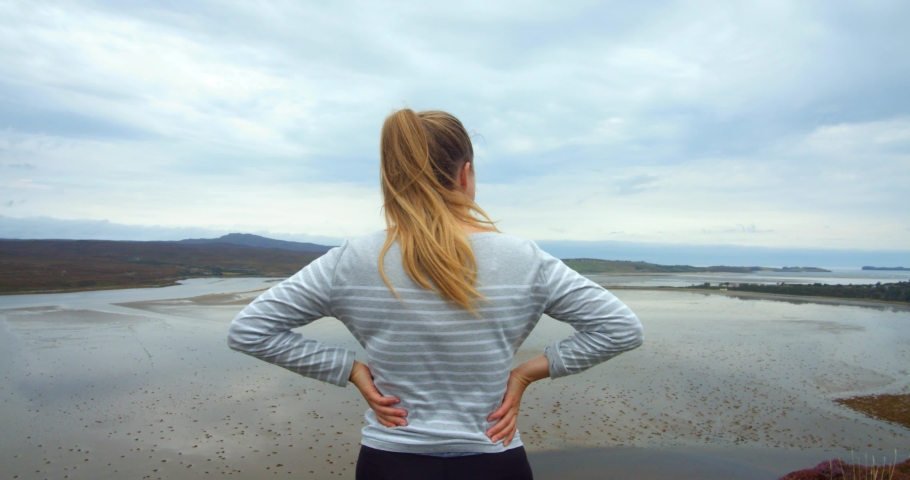 Slow Motion. Young blonde Finnish woman walking on top of a cliff looking out over the ocean in the Scottish Highlands travelling the NC500.