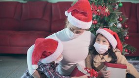 the family wearing the protective mask and opening gift boxes during the Christmas festival celebration. the concept of coronavirus, pandemic, Christmas and gifts.