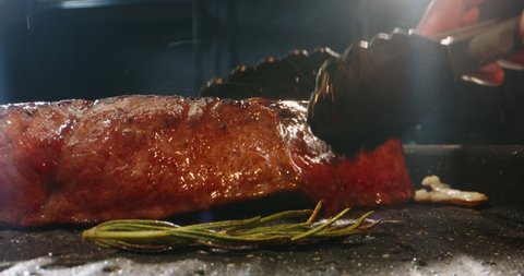 Close up shot of juicy beef steak being roasted in kitchen. Chef flipping a tasty piece of meat. Steak being cooked and prepared 4k footage