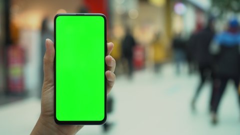 Shopping center. Department store. Mall. Back view of brunette holding chroma key green screen smartphone watching content. Shopping online. Gadgets and contemporary people concept.