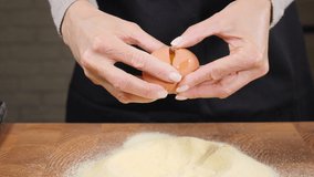 Female hands breaking egg into powder. Slow motion. Cracking raw egg while making dough for pasta or pastry in home kitchen. Food video. Baker kneading dough for cake. Full hd