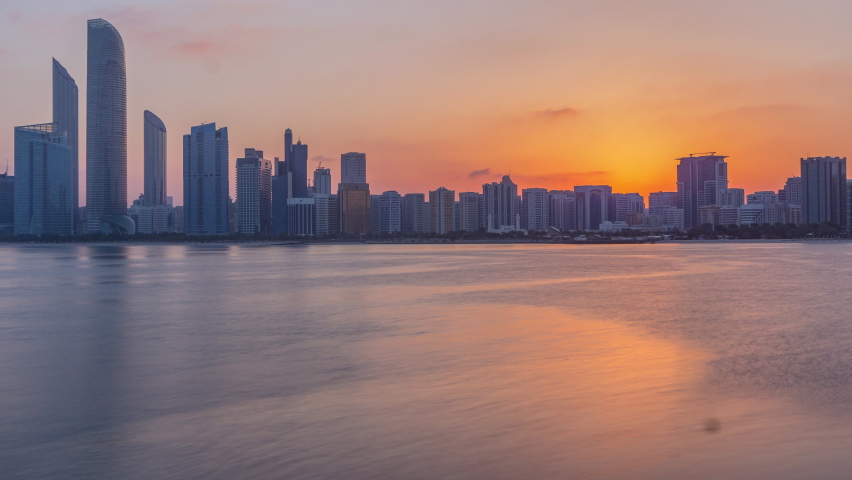 Abu Dhabi city skyline on sunrise time with water reflection timelapse from the breakwater near cultural village. Few clouds on morning sky | Shutterstock HD Video #1063746886