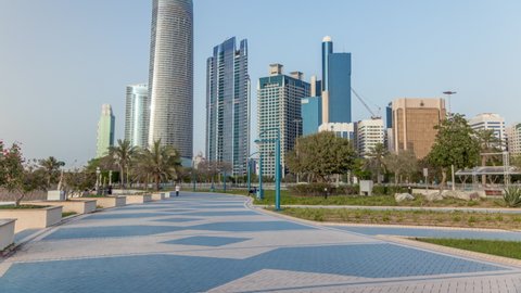 Corniche boulevard beach park along the coastline in Abu Dhabi timelapse with skyscrapers on background. Palms on a side. Blue sky at sunny day