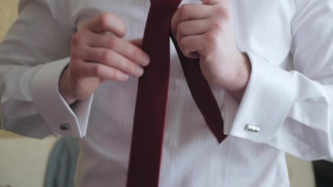 A man in a white shirt ties a red tie around his neck. learning tying a necktie