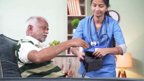 Nurse of doctor busy in setting up BP or blood pressure medical equipment to senior man at home of check up at home - concept of routine home help check.