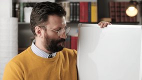 Online education and distance learning concept. Male English teacher talking and looking at camera and writing English words on white magnetic marker board, man is at workplace at home or in office