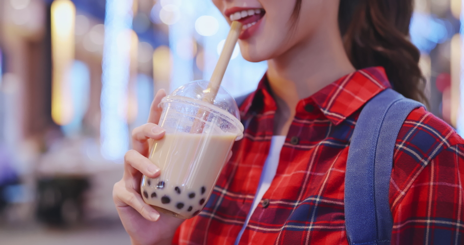 close up of smiling asian woman holds a cup of tapioca ball tea at city night while on vacation