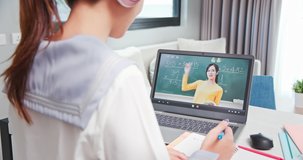 rear view of asian girl is learning math and looking elementary school female teacher teaching online through laptop at home