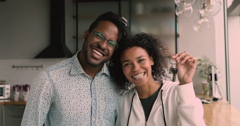African couple standing in kitchen smile look at camera, happy wife show bunch of keys from new luxury house. Young family happy homeowners portrait, rented flat, loan mortgage, relocation day concept