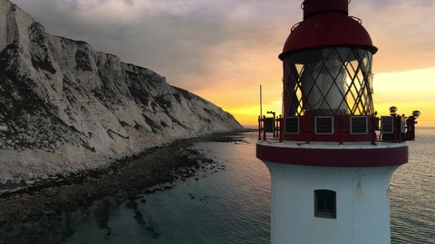 Landscape aerial drone footage video of a Beachy Head Lighthouse and chalk cliffs at colorful sunrise with low tide in England, near Eastbourne.