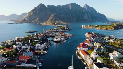 Drone shot over a catamaran arriving in the Henningsvaer village, sunny evening, Lofoten, Norway - reverse, aerial view