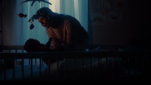 Authentic Footage of a Cute Newborn Baby Boy Lying on the Back in Child Crib in a Dark Room. Mother Picks Up Neonate Toddler from the Bed. Concept of Childhood, New Llife, Parenthood.