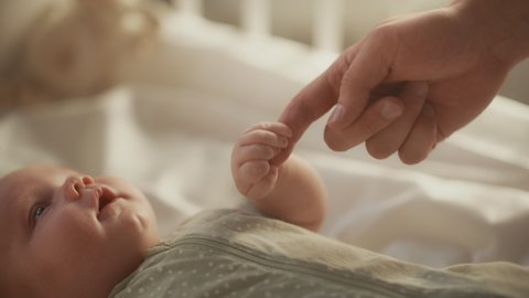 Close Up Footage of Newborn Baby Playing With Mother's Hand and Finger while Lying on the Back in Child Crib. Caucasian Neonate Toddler Bodning with Mom. Concept of Childhood, New Llife and Parenthood