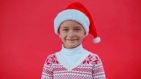 smiling girl in santa hat and christmas sweater isolated on red