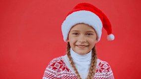 girl in santa hat and christmas sweater playing with braids isolated on red