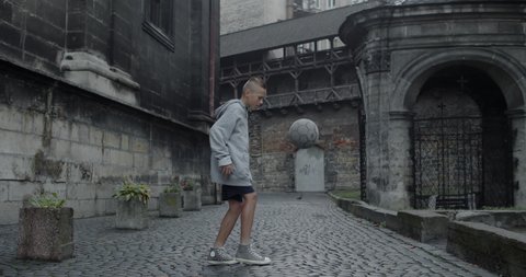 Capable teenager guy kicking football ball with feet . Young talanted boy s practicing tricks at old european city street. Concept of sport, talent and lifestyle.