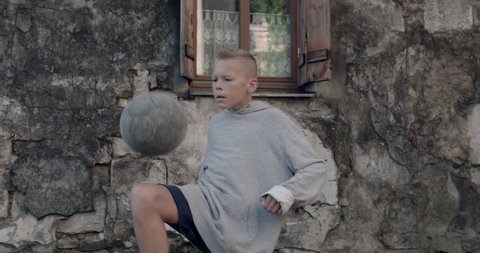 Crop view of teen boy kicking soccer ball with knee. Talanted kid practicing tricks. Old damaged building facade at background. Concept of sport and lifestyle.