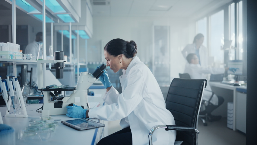 Medical Development Laboratory: Portrait of Beautiful Caucasian Female Scientist Looking Under Microscope, Analyzes Petri Dish Sample. People do Medicine, Biotechnology Research in Advanced Lab | Shutterstock HD Video #1063773001