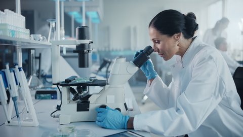 Medical Development Laboratory: Portrait of Beautiful Caucasian Female Scientist Looking Under Microscope, Analyzes Petri Dish Sample. People do Medicine, Biotechnology Research in Advanced Lab