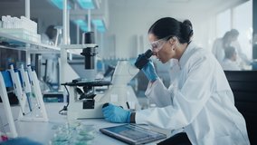 Medical Development Laboratory: Portrait of Beautiful Caucasian Female Scientist Looking Under Microscope, Analyzes Petri Dish Sample. People do Medicine, Biotechnology Research in Advanced Lab - Powered by Shutterstock - Get 15% off with code: PIKWIZARD15