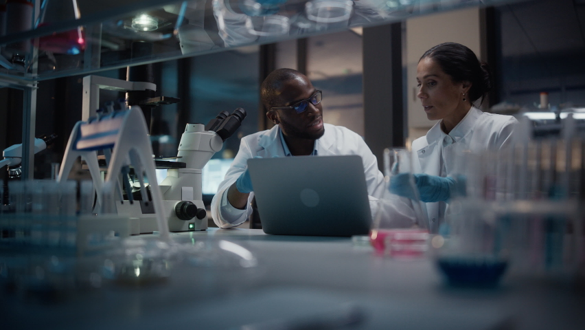 Modern Medical Research Laboratory: Caucasian and Black Scientists Work on Laptop, Do Data Analysis, Talk. Advanced Scientific Pharmaceutical Lab for Medicine, Biotechnology Development. Evening Time | Shutterstock HD Video #1063773106