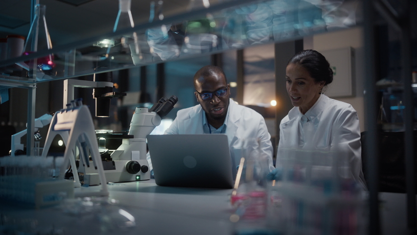 Modern Medical Research Laboratory: Caucasian and Black Scientists Work on Laptop, Do Data Analysis, Talk. Advanced Scientific Pharmaceutical Lab for Medicine, Biotechnology Development. Evening Time - Powered by Shutterstock - Get 15% off with code: PIKWIZARD15