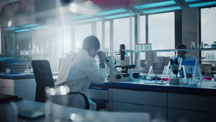 Medical Development Laboratory: Back View of Japanese Male Scientist Using Touch Screen Digital Tablet Computer, Doing Data Analysis Research. Biotechnology Specialists in Advanced Scientific Lab Royalty-Free Stock Footage #1063773172