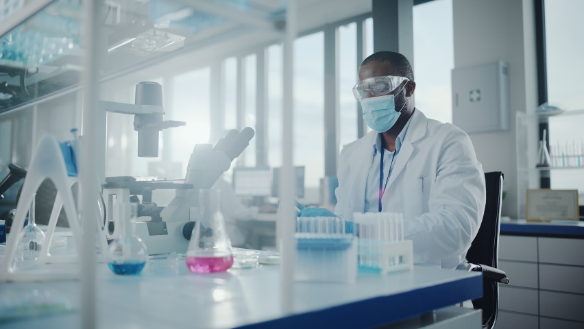 Medical Development Laboratory: Black Scientist wearing Face Mask Uses Pipette for Filling Test Tube with Liquid, Conducting Experiment. Pharmaceutical Lab with Medicine, Biotechnology Researchers Royalty-Free Stock Footage #1063773229