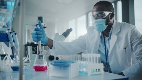 Medical Development Laboratory: Black Scientist wearing Face Mask Uses Pipette for Filling Test Tube with Liquid, Conducting Experiment. Pharmaceutical Lab with Medicine, Biotechnology Researchers