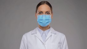 medicine, profession and healthcare concept - video portrait of female doctor or scientist in white coat and medical mask showing thumbs up mask over grey background